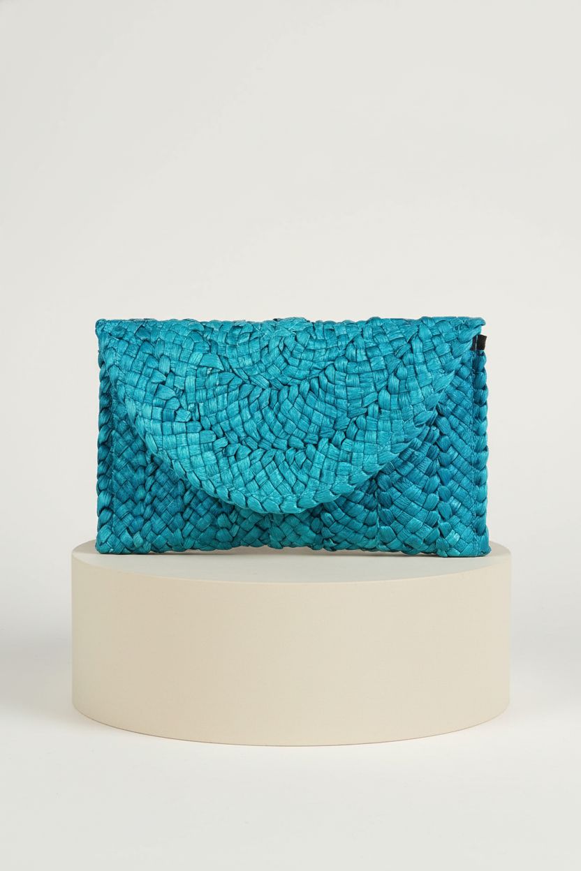 KUANG! turquoise straw envelope clutch showcased on a matte pedestal with soft studio lighting.