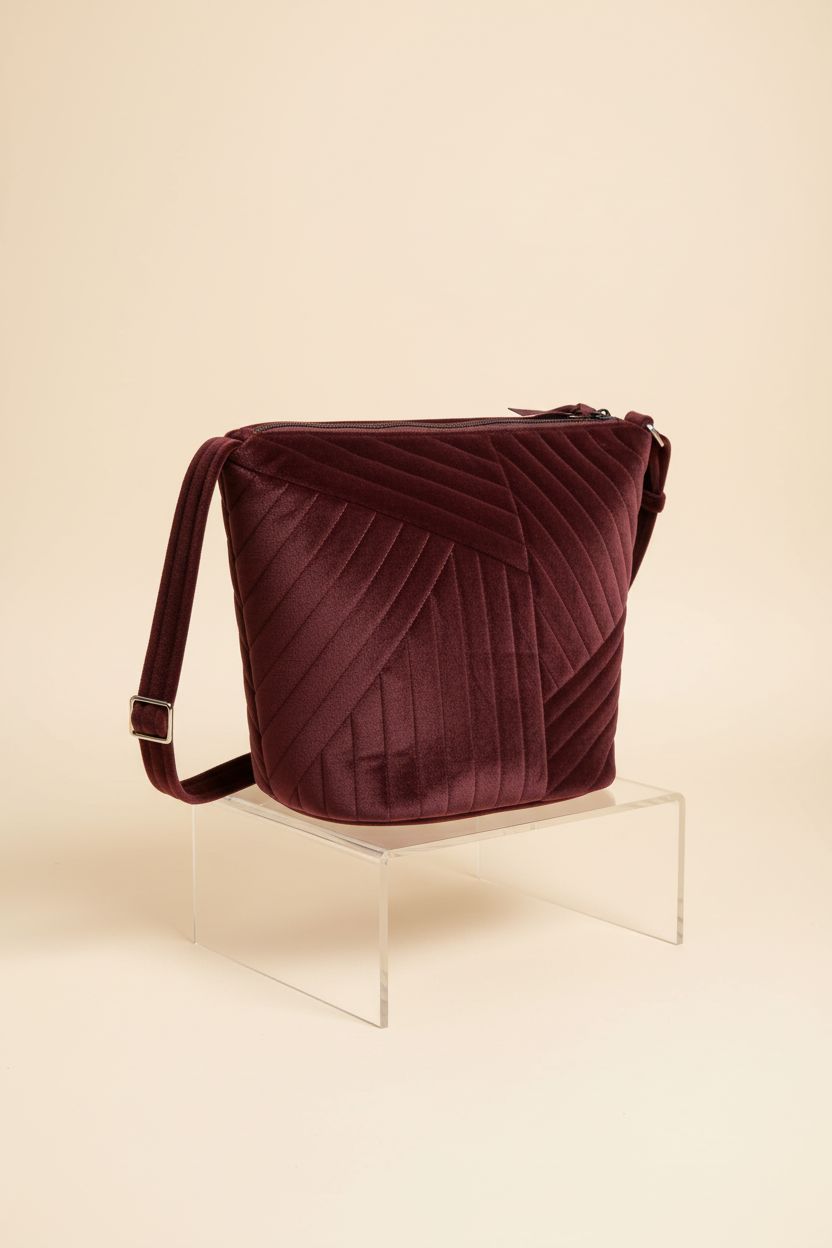 Vera Bradley raisin velvet bucket purse displayed on a warm-cream background, highlighting its design.