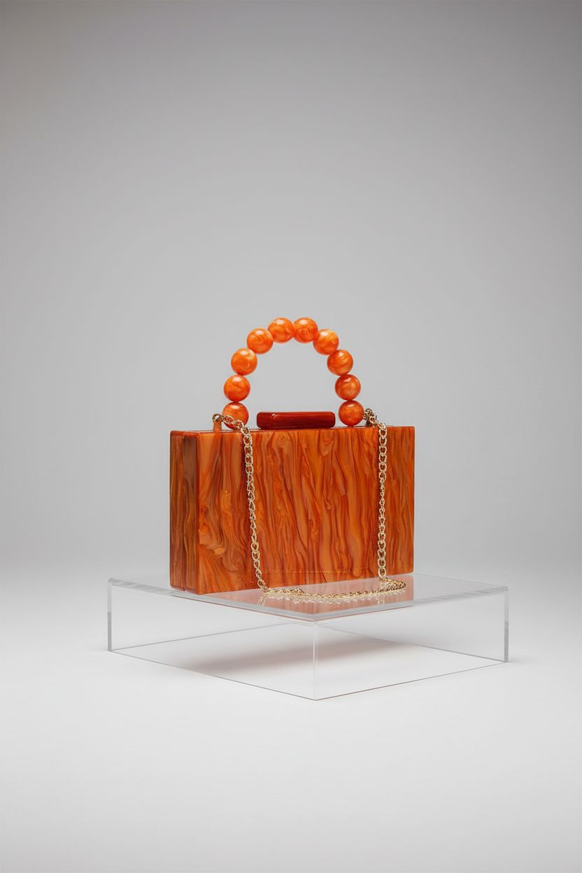 Product shot of Jessie burnt orange acrylic clutch with gold chain and pearl handle.