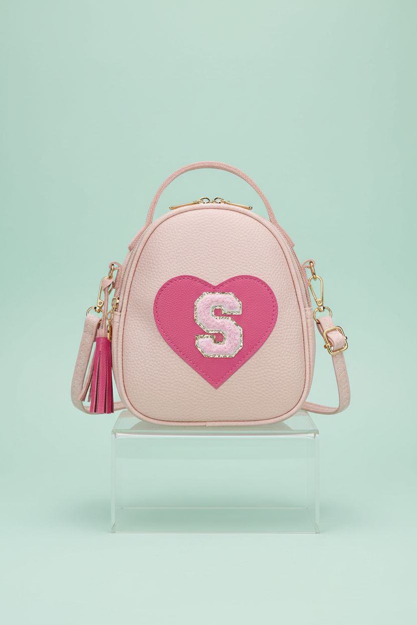 KKXIU blush-pink purse with gold hardware and sequined initial on a mint backdrop.